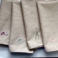 four linen napkins with embroidered letters on them sitting next to each other in a row