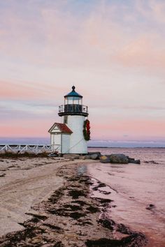 a light house sitting on top of a sandy beach next to the ocean at sunset