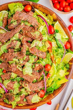 a salad with beef, lettuce and tomatoes in a wooden bowl on a white table