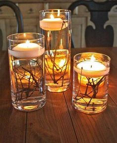 three glass vases filled with candles on top of a wooden table