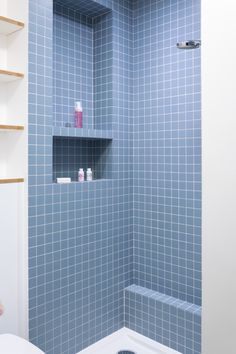 a blue tiled shower with shelves above it