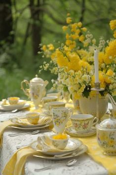 the table is set with yellow flowers and tea cups