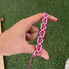 a hand holding a pink and white bracelet on top of a green grass covered field