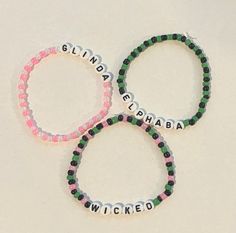 These are Wicked inspired bracelets. Wicked the Movie and Wicked the Musical Bracelets! Elphaba and Glinda Bracelet! You can also get a custom wicked inspired set where you tell me what you want on five bracelets! The bracelets are all made with stretch cord or elastic cord. Colors are mostly associated with the color themes of Wicked! Each order will have colors that are the same or similar to the pictures. These are homemade and perfect for wearing to the wicked movie or musical show. If you have any questions, send me a message. If you want the bracelets sooner, message me and I'll let you know if it's possible. Note that these are regular bracelets so if you stretch them too much they will break, they are meant to go over your hand onto your wrist/arm. The bracelets are 7-7.5 inches. I Wicked Friendship Bracelet, Wicked Bracelet Ideas, Wicked Bracelet, Bracelet Homemade, Wicked Movie, Elphaba And Glinda, Wicked The Musical, Movie Crafts, Inspired Bracelets