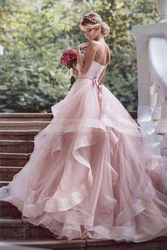 a woman in a pink wedding dress standing on steps with her back to the camera