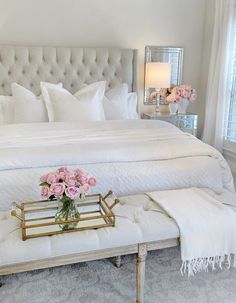 a bed with white linens and pink flowers in a vase on the end table