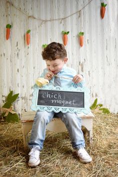 a young boy is sitting on a bench holding a chalkboard that says chick magnet