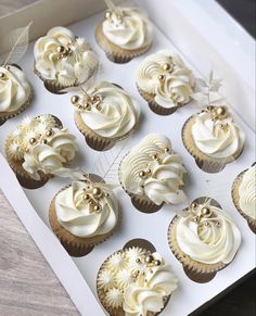 cupcakes with white frosting and gold decorations in a box on a table