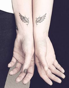 two people with matching tattoos on their arms holding each other's hands and one has an angel tattoo on it