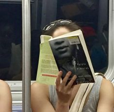 a woman reading a book while sitting on a subway train with her head covered by a paper