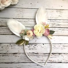 a white headband with flowers and feathers on top of a wooden table next to roses