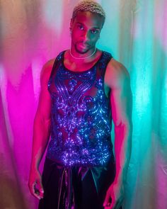 Introducing our men's sleeveless top, crafted from sheer black mesh fabric and adorned with intricate blue sequins. The sequins form elaborate, symmetrical patterns that cover most of the front, giving the top a sparkling and eye-catching appearance. Perfect for festivals, night outs, or any occasion where you want to stand out, this tank top combines edgy style with detailed craftsmanship. Add a touch of glamour and uniqueness to your wardrobe with this stunning piece. Black Contrast Sequin Fabric, Fitted Blue Vest For Party, Sequin Sleeveless Tank Top For Club, Blue Party Vest Top, Blue Stretch Tank Top For Party, Festival Sleeveless Sequined Tops, Stretch Festival Tops With Sequins, Blue Tank Top For Party, Blue Sheer Tops For Party