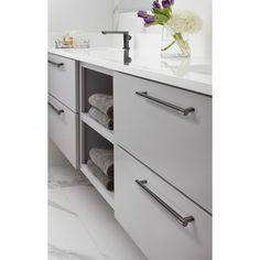 a white bathroom with marble counter tops and drawers, along with towels on the shelf