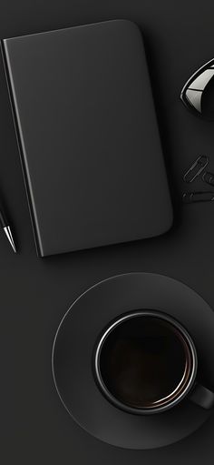 a cup of coffee next to a notebook and pen on a black surface with writing utensils