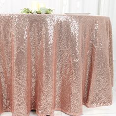 a gold sequin tablecloth with two candles on it and flowers in the center