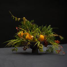 a vase filled with fruit and greenery on top of a table