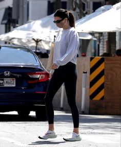 a woman walking down the street in black leggings and a white shirt with an oversized collar