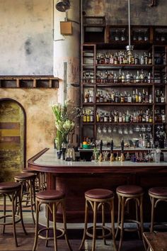 an old bar with stools and shelves full of bottles on the wall behind it