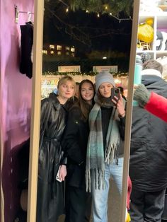 three women standing in front of a mirror taking a selfie with their cell phone