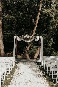 an outdoor ceremony setup with white chairs and flowers on the aisle, surrounded by trees