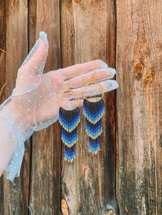 a pair of blue and gold beaded earrings hanging from the palm of a person's hand