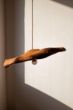 a piece of wood hanging from a string on a wall next to a white wall