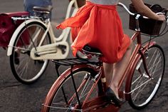 a woman in an orange dress is riding a red bike with two bicycles behind her