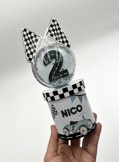 a hand holding up a cup with the number two on it and a race car design