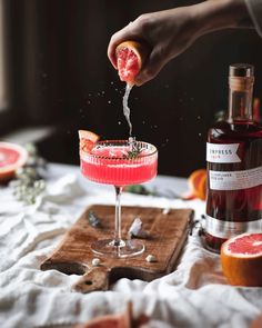 a person is sprinkling grapefruit into a pink cocktail with blood oranges