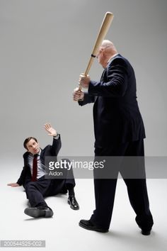 a man holding a baseball bat while another man sits on the ground in front of him