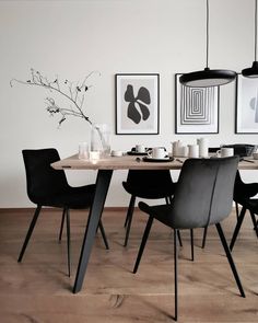 a dining table with black chairs and pictures on the wall above it in a white room