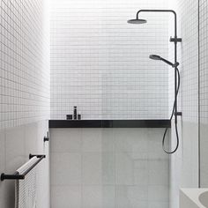 a white tiled bathroom with black accents and accessories on the shower head, sink, and toilet