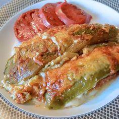 a white plate topped with meat covered in sauce next to tomato slices and green beans