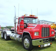 a large red truck parked on top of a lush green field next to other trucks