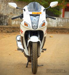 a white motorcycle parked on top of a dirt road next to a building and trees