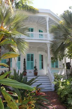 a white house with green shutters and palm trees in front of the porch area