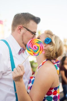 a man and woman kissing while holding a lollipop