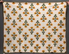 an orange and green quilt hanging on a wall with two hands holding it up to the camera