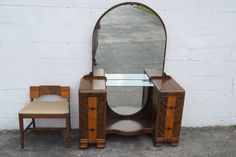 an antique vanity with mirror and chair in front of a white brick wall on the street