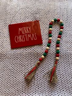 a red merry christmas sign sitting on top of a table next to a beaded necklace