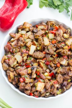 a white bowl filled with meat and vegetables next to a red pepper on the side