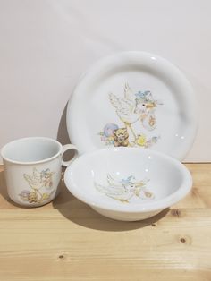 two white dishes with cup and saucer sitting on a wooden table next to each other