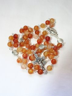 "This Catholic Carnelian rosary is made with 8mm light orange gemstone rounds. It is a larger size, 5 decade rosary. It measures about 31 inches around with a 6\" cross extension. I hand turned the silver plated wires. 10mm flat, carved, pewter rounds were used for the Pater beads. The crucifix is Italian made oxidized silver. It has a Miraculous medal connector. This rosary will be slipped into a velvet bag and shipped in a bubble mailer." Healing Rosary With Miraculous Medal And Round Beads, Healing Rosary With Miraculous Medal, Crucifix Rosary With 8mm Beads For Meditation, 8mm Bead Crucifix Rosary For Meditation, Silver Rosary With 8mm Beads For Healing, Silver Rosary With Round Beads For Meditation, Silver Rosary With Natural Stones, Silver Rosary With Natural Stones And Round Beads, Blue Spot Jasper