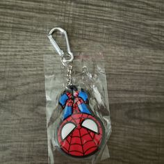 a spiderman shaped keychain is in plastic on a wooden table with a clear bag