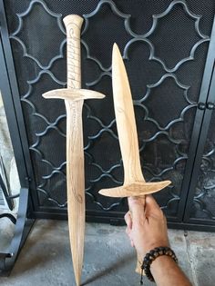 a hand holding two wooden swords in front of a fireplace