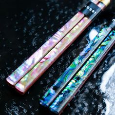 two different colored pens sitting next to each other on top of a black surface with drops of water