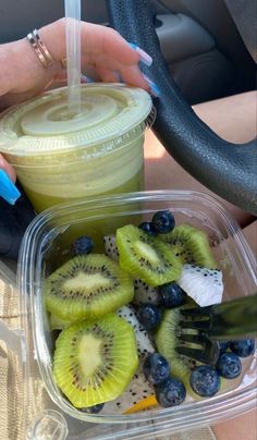 a person holding a plastic container filled with kiwis and blueberries next to a cup of smoothie