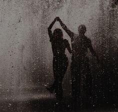 two people standing in the rain with their hands up and one person holding an umbrella