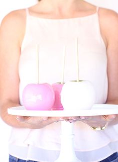 a woman holding a white plate with two apples on top of it and toothpicks in the middle