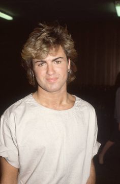 a man with blonde hair wearing a white t - shirt and looking at the camera